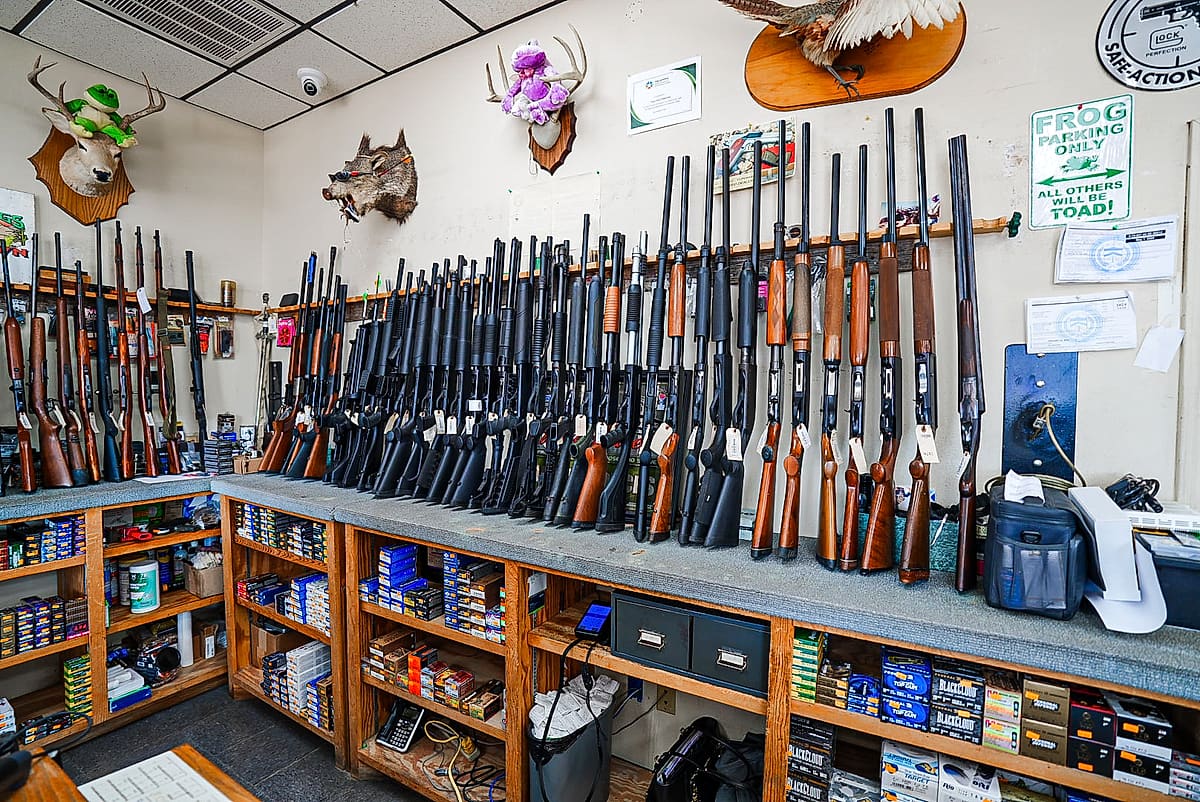 Wall racks of rifles and shotguns above shelves of ammunition